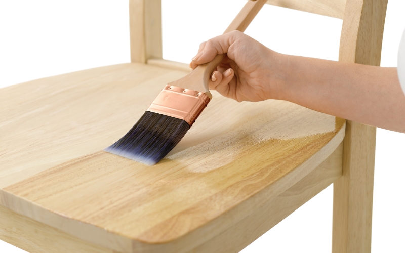 Hand applying clear wood stain on a wooden chair with a brush